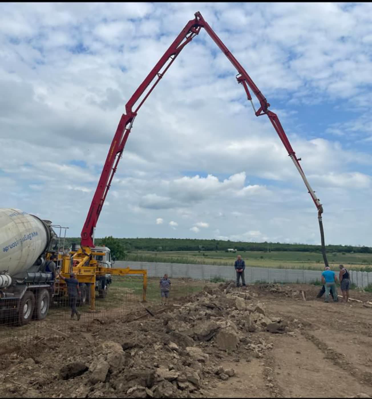 Pompă de beton cu brațul desfășurat la o lucrare pe teren deschis